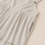 Close-up of a brown strap button, gathered fabric and side pocket on a light jumpsuit