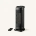 Black tower heater with a front grille, top control panel and a remote beside the base