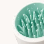 Close-up de cerdas cor de menta dentro de um copo branco para limpar patas, com gotas de água visíveis