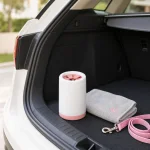 Copo branco e rosa para limpar patas junto de uma toalha cinzenta e de uma trela rosa na bagageira aberta de um carro