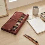 Trousse à pinceaux marron foncé partiellement enroulée, avec pinceaux près d'un carnet de croquis, de crayons et d'une tasse