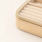 Close-up of the cream jewelry case corner showing ring rolls, a gold-tone zipper and edge stitching