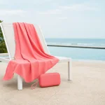 Toalla coral colocada sobre una silla blanca junto a la piscina, con una funda a juego en el suelo