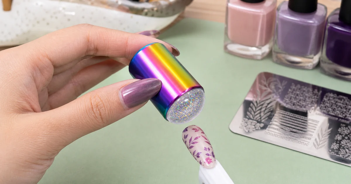 Estampador de uñas arcoíris con cabezal transparente sobre una uña de práctica pintada