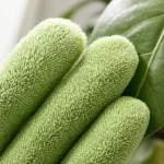 Primo piano delle dita di un guanto verde, con superficie densamente testurizzata accanto a una foglia
