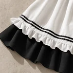 Close-up of the white apron hem with two parallel black ribbons and a white ruffle layered over the black skirt.
