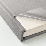 Close-up of the gray album cover, white page edges and a lifted transparent overlay