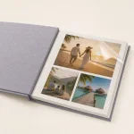 Open gray photo album with beach and travel photos beneath a partly lifted clear sheet