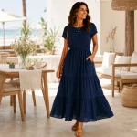Frau in marineblauem Maxikleid auf einer überdachten Terrasse, eine Hand in der Seitentasche