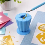 Weeding hook placing a yellow vinyl scrap into a blue slotted collector