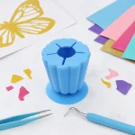 Blue vinyl scrap collector beside a weeding hook, tweezers and cut vinyl pieces