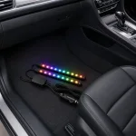 Two illuminated light strips and their controller laid in a car's front passenger footwell.
