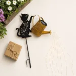 Leuchtende Gießkanne und katzenförmiger Erdstecker neben Blumen und einem verpackten Geschenk