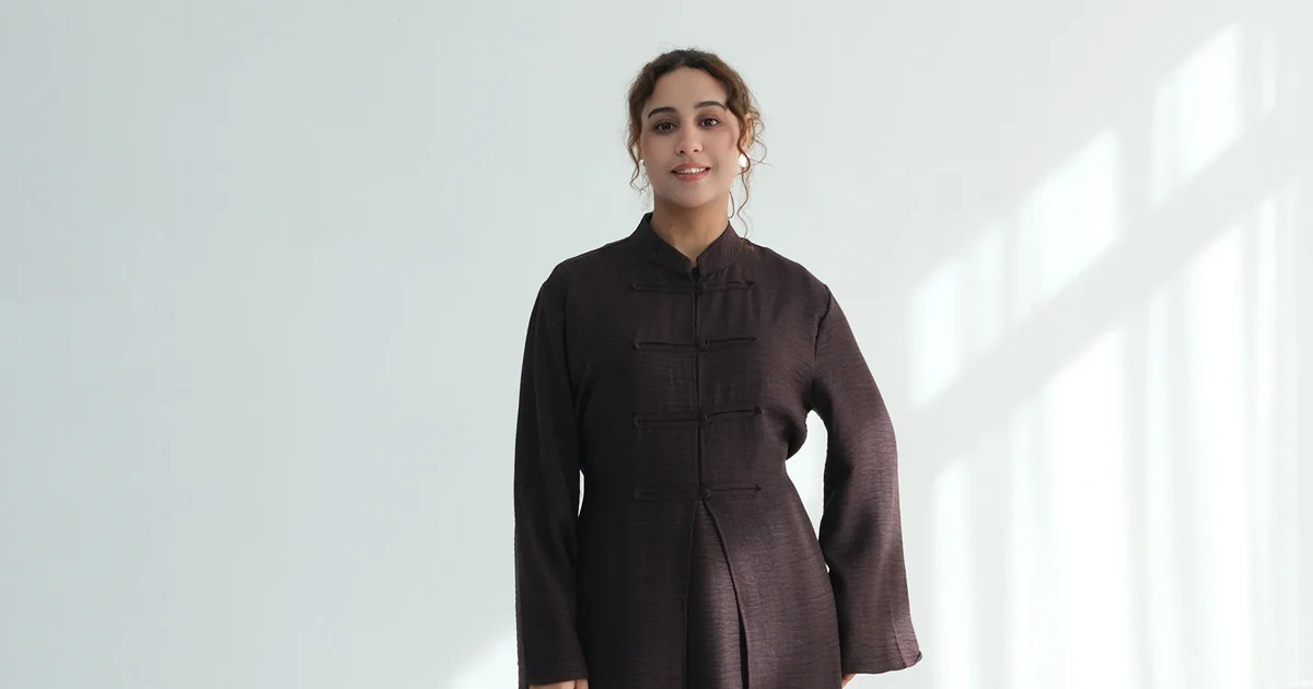 Modella con abito lungo color caffè, collo alto, chiusura davanti e spalle visibili