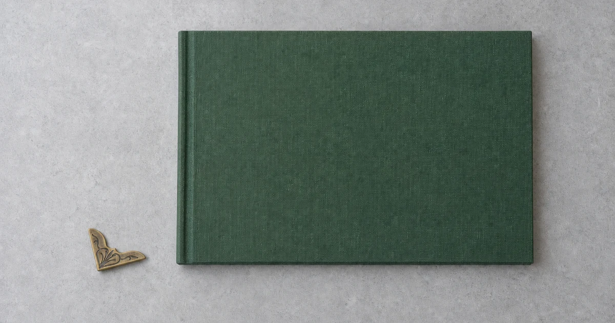Uma única cantoneira decorativa de ferro com acabamento bronze ao lado de um caderno verde de tecido sem peças metálicas