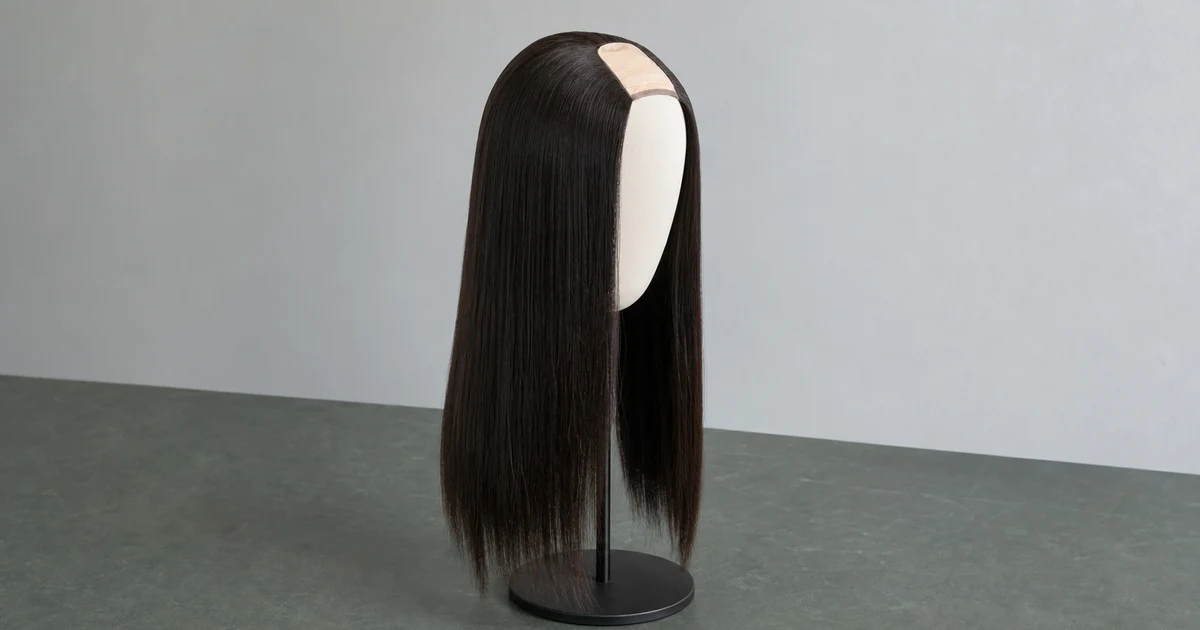 Peluca U-part negra y lisa con la abertura de la coronilla visible, sobre una cabeza de exposición blanca y un soporte negro.