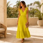 Frau in gelbem Maxikleid mit Bindeträgern auf einer Terrasse und einer geflochtenen Clutch