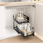 Black organizer beneath a kitchen sink holding bottles, sponges and folded cloths in two tiers