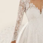 Primo piano di maniche in pizzo floreale, scollo smerlato e vita di un abito da sposa bianco