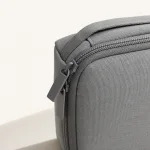 Close-up da bolsa cinzenta com superfície texturada, dentes do fecho, puxador e alça cosida