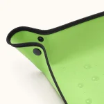 Gros plan sur un coin du tapis vert, avec boutons-pression, bordure noire et gouttes d'eau