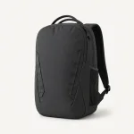 Vista frontal inclinada de mochila escura com duas alças superiores, costuras diagonais e bolso lateral de tela