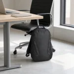 Mochila escura ao lado de uma cadeira de escritório e uma mesa com laptop