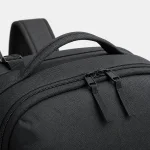 Close da mochila escura mostrando as alças superiores, os puxadores duplos do zíper e a textura do tecido