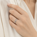 La mano di una donna adulta indossa un anello color argento a linee incrociate, con una camicia color avorio sullo sfondo.