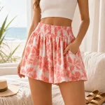 Woman wearing coral floral shorts with a white cropped top, one hand in a side pocket