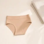 Beigefarbene Unterhose flach neben einem gefalteten hellen Handtuch ausgelegt