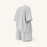 Vista trasera en ángulo de camiseta gris claro y shorts con hombros caídos y mangas holgadas