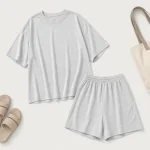 Camiseta gris claro y shorts extendidos junto a sandalias y una bolsa tote