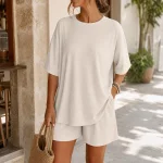 Woman wearing an off-white ribbed top and shorts while holding a woven bag outdoors