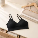Black ribbed bralette on a dresser beside folded clothes and a wooden hanger