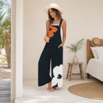 Frau in marineblauem Jumpsuit mit Blumenmuster und weitem Bein und Strohhut, eine Hand in der Tasche