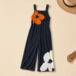 Flach ausgelegter marineblauer Jumpsuit mit Blumenmuster und weitem Bein neben Strohhut und Sandalen