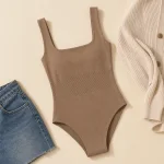 Flach ausgelegter taupefarbener Body mit eckigem Ausschnitt neben blauen Jeans und einer cremefarbenen Strickjacke