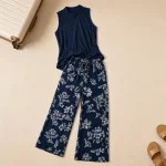 Top blu navy semplice e pantaloni floreali stesi accanto a una borsa da viaggio e sandali
