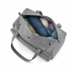 Borsa grigia aperta per filati piena di gomitoli colorati, con manici e occhielli metallici