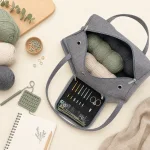 Vista dall'alto di una borsa grigia aperta per filati e custodia per uncinetti, accanto a filati, forbici e taccuino