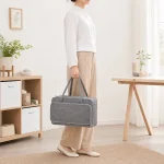 Persona che tiene una borsa artigianale grigia chiusa per i manici, in piedi al chiuso