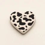 Low-angle detail of a cream heart charm with black cow-print patches