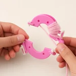 Hands winding pale pink yarn around the curved arms of a pink plastic maker.