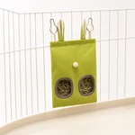 Sac à foin vert suspendu aux barreaux blancs d'un enclos, avec du foin visible par les deux ouvertures avant