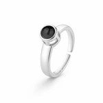 Anillo abierto de color plateado con lente redonda oscura, en ángulo sobre blanco