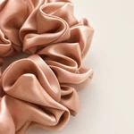 Gros plan sur un chouchou rose montrant les plis du tissu légèrement brillants et la bordure cousue