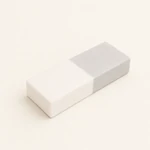 Rectangular cleaning eraser with white and light gray sections on a pale surface