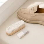 White-finned cleaning brush and two-tone eraser placed beside a beige slip-on shoe
