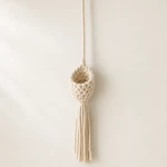 Three-quarter view of an empty beige cotton-rope hanger showing its woven basket and fringe.